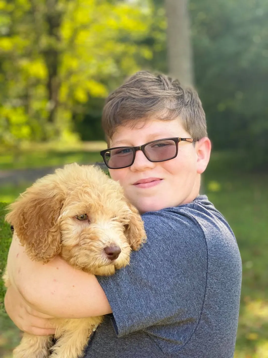 Boy in glasses hugging an apricot Goldendoodle puppy outdoors in autumn light